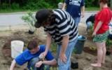 person using spade to smooth dirt around plant while others look on